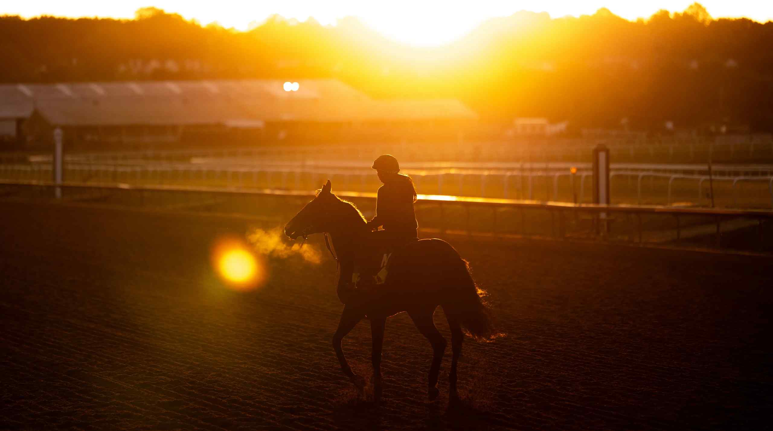 A sun setting on a lone horse rider on a course.